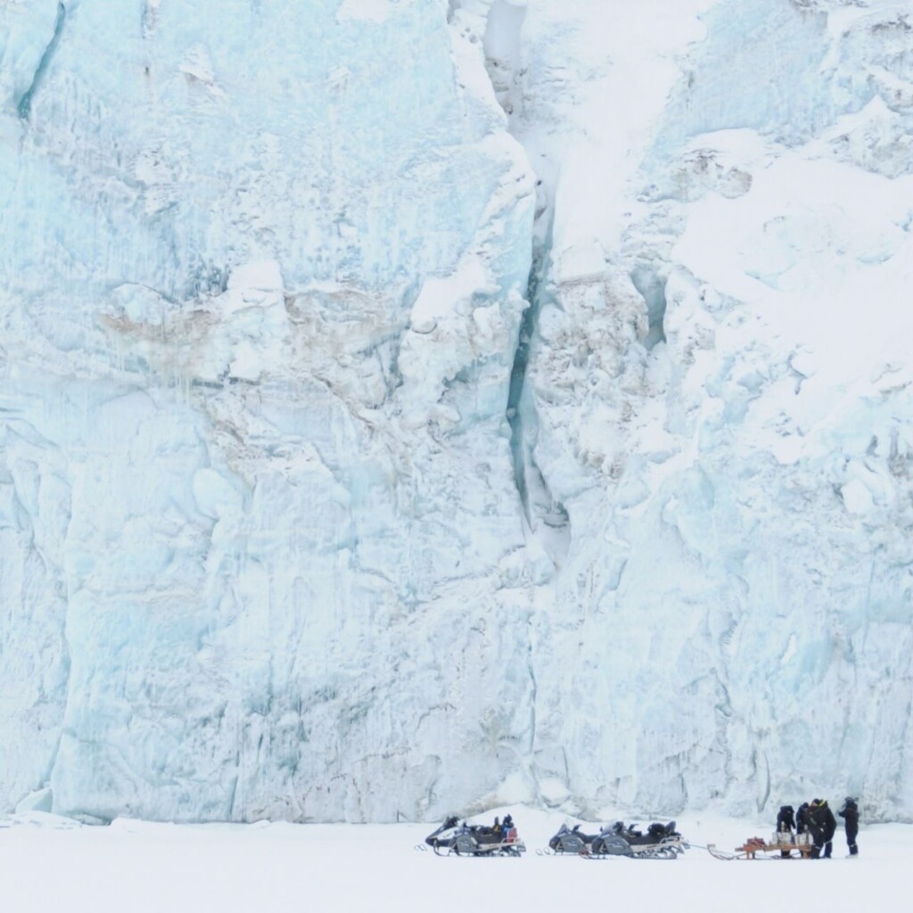 Blauwe ijsmassa in Spitsbergen met daarvoor een groep mensen met sneeuwscooters.